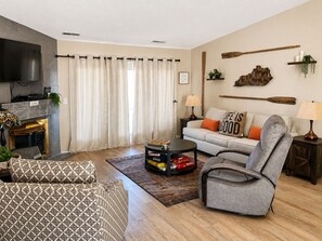 A living room with a sofa, armchair, coffee table, fireplace, and a television.