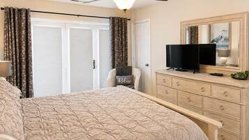 A bedroom with a bed, a television on a dresser, a ceiling fan, and a door with curtains.