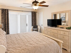 A bedroom with a bed, a television on a dresser, a ceiling fan, and a door with curtains. - One Bedroom Harbor View Condo (Grand Rivers)