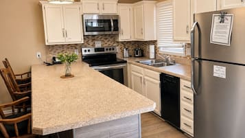 A kitchen with white cabinets, stainless steel appliances, a granite countertop, and a wooden dining set.