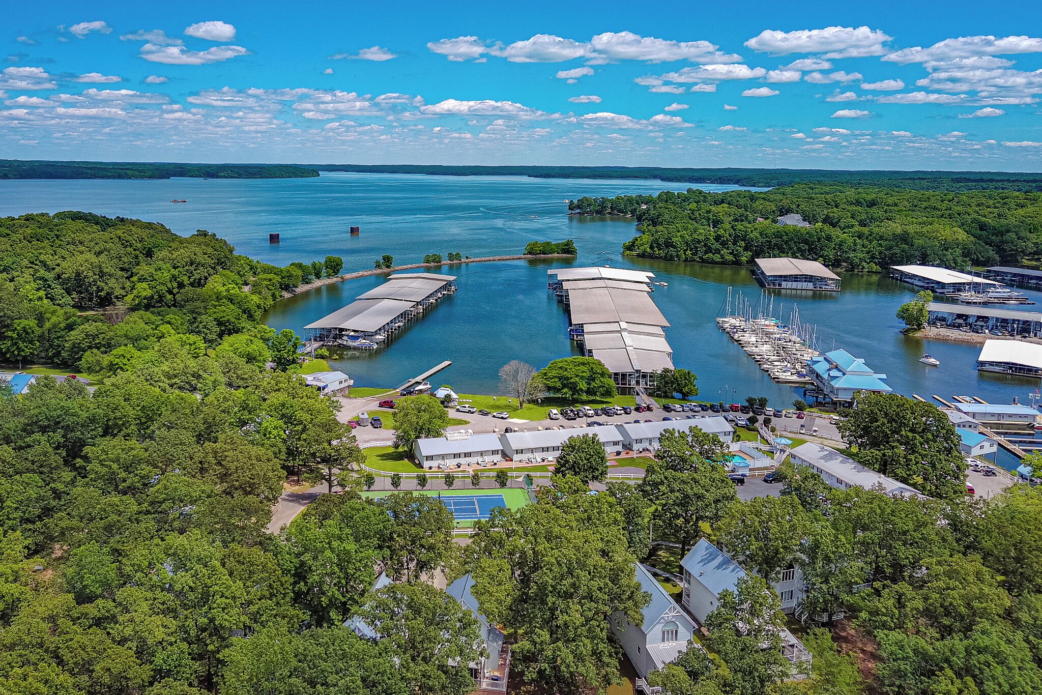 A marina with docked boats, a tennis court, and surrounding greenery.