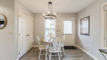 A dining area with a round table and white chairs, a chandelier, and a door with a window.