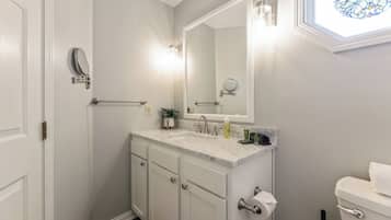 Une salle de bain avec un meuble-lavabo blanc, un grand miroir, des toilettes et une fenêtre ornée de vitraux.