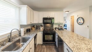 Una cucina moderna con mobili bianchi, piani di lavoro in granito, forno a microonde integrato, fornello, forno e lavello.