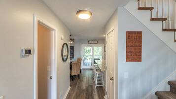 A hallway with a staircase, a dining area with wicker chairs, and a sign listing Lake House rules.