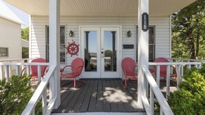 A covered porch with white railings and red chairs, a ship's wheel decoration, and a mailbox. - Two Bedroom Harbor View Condo (Grand Rivers)