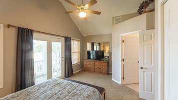 A bedroom with a bed, a ceiling fan, a dresser, a television, and a door leading to another room.