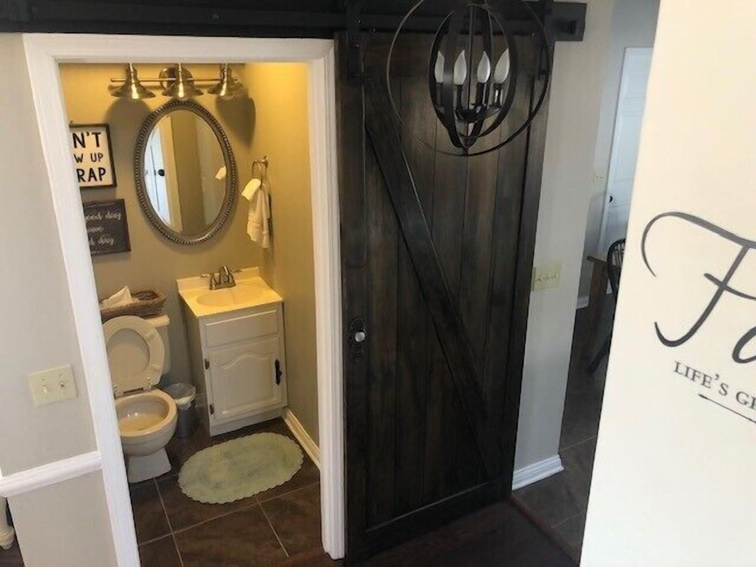 A bathroom with a toilet, sink, and mirror. There is a sign that says "N'T W UP RAP" and another sign with text that is not fully visible.
