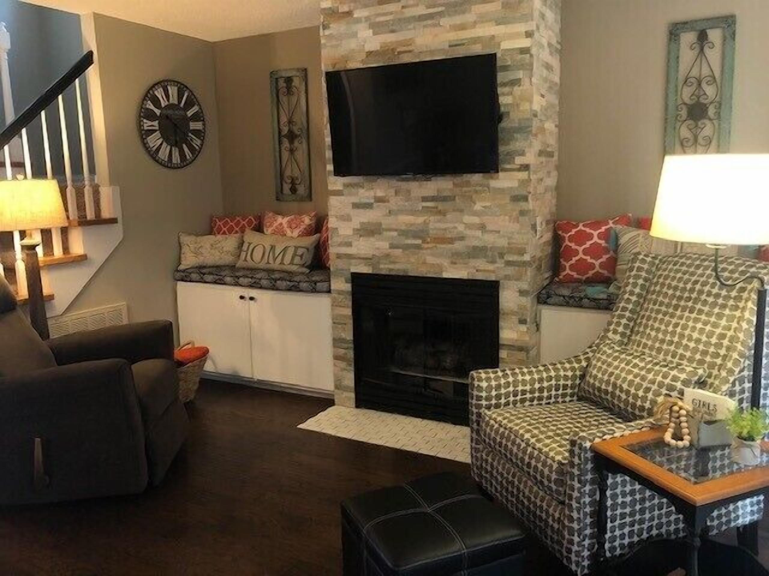 A living room with a fireplace, a television mounted above it, a sofa, and a chair.
