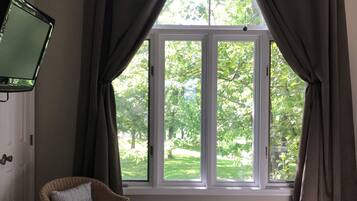 A room with a bed, a chair, a television, and a window with curtains.