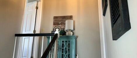 A staircase with a white door at the top, a teal cabinet with a lamp, and a wall-mounted picture.
