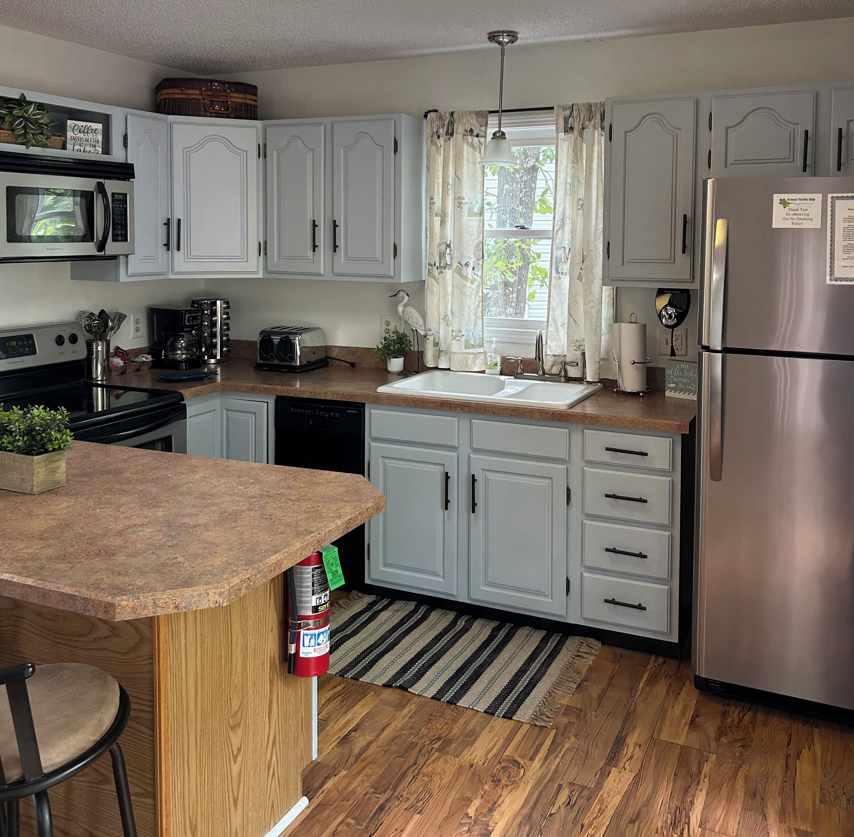 A kitchen with white cabinets, a stainless steel refrigerator, a microwave, a toaster, and a sink.
