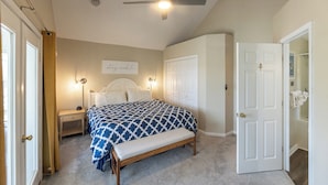 A bedroom with a bed, bedside tables, a bench, a ceiling fan, and a door leading to a bathroom.