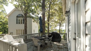 A wooden deck with a table and chairs, a barbecue grill, and a white house in the background.