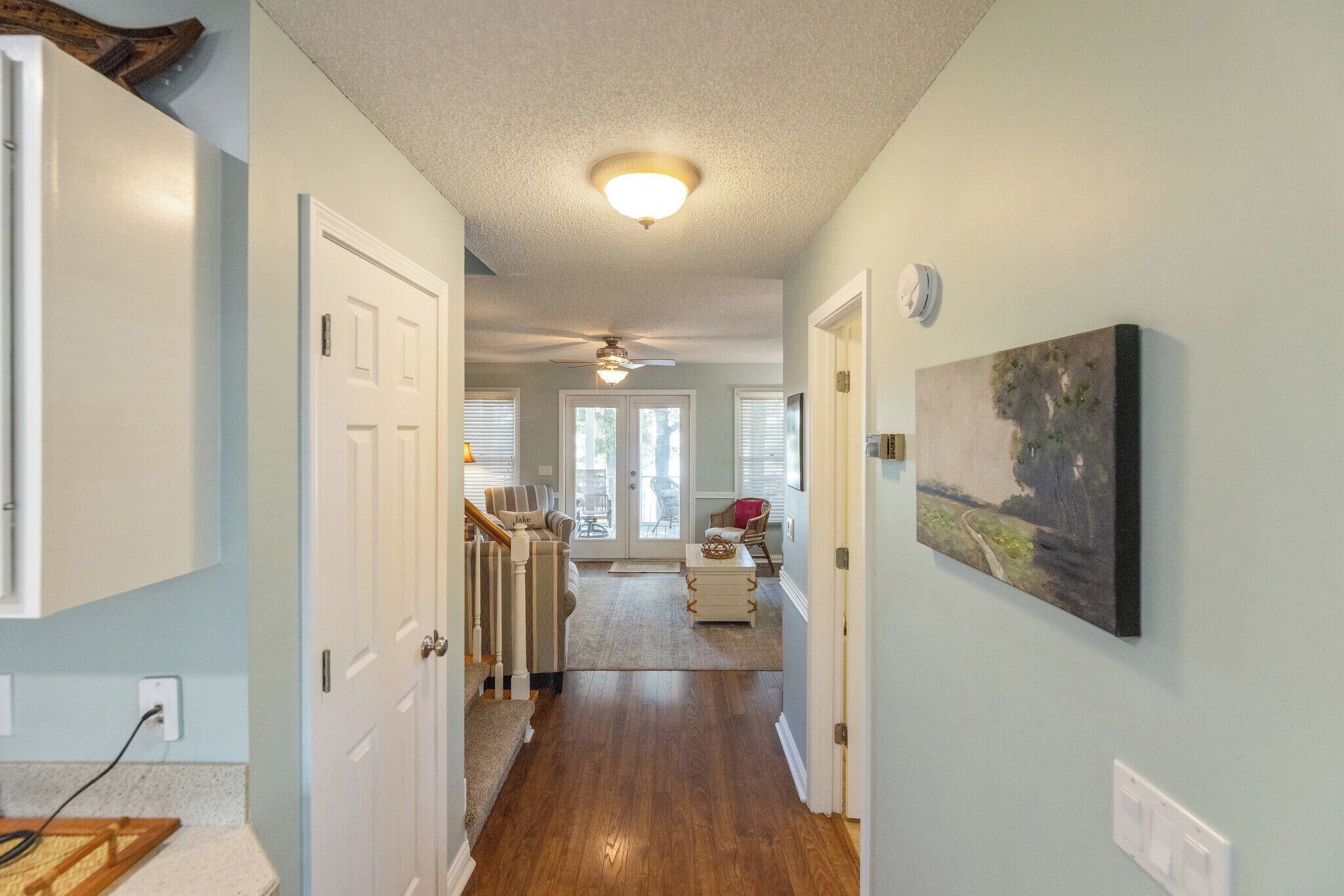 A hallway with wooden flooring, white doors, a ceiling fan, and a painting on the wall.