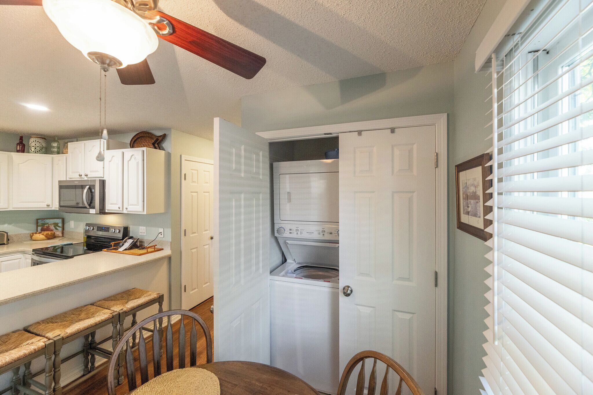 A compact kitchen with white cabinets, a built-in microwave, and a dining area with a bench and chairs.
