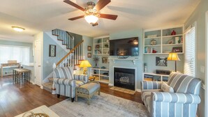 A living room with a fireplace, striped armchairs, a television, and a bookshelf. - Two Bedroom Harbor View Condo (Grand Rivers)