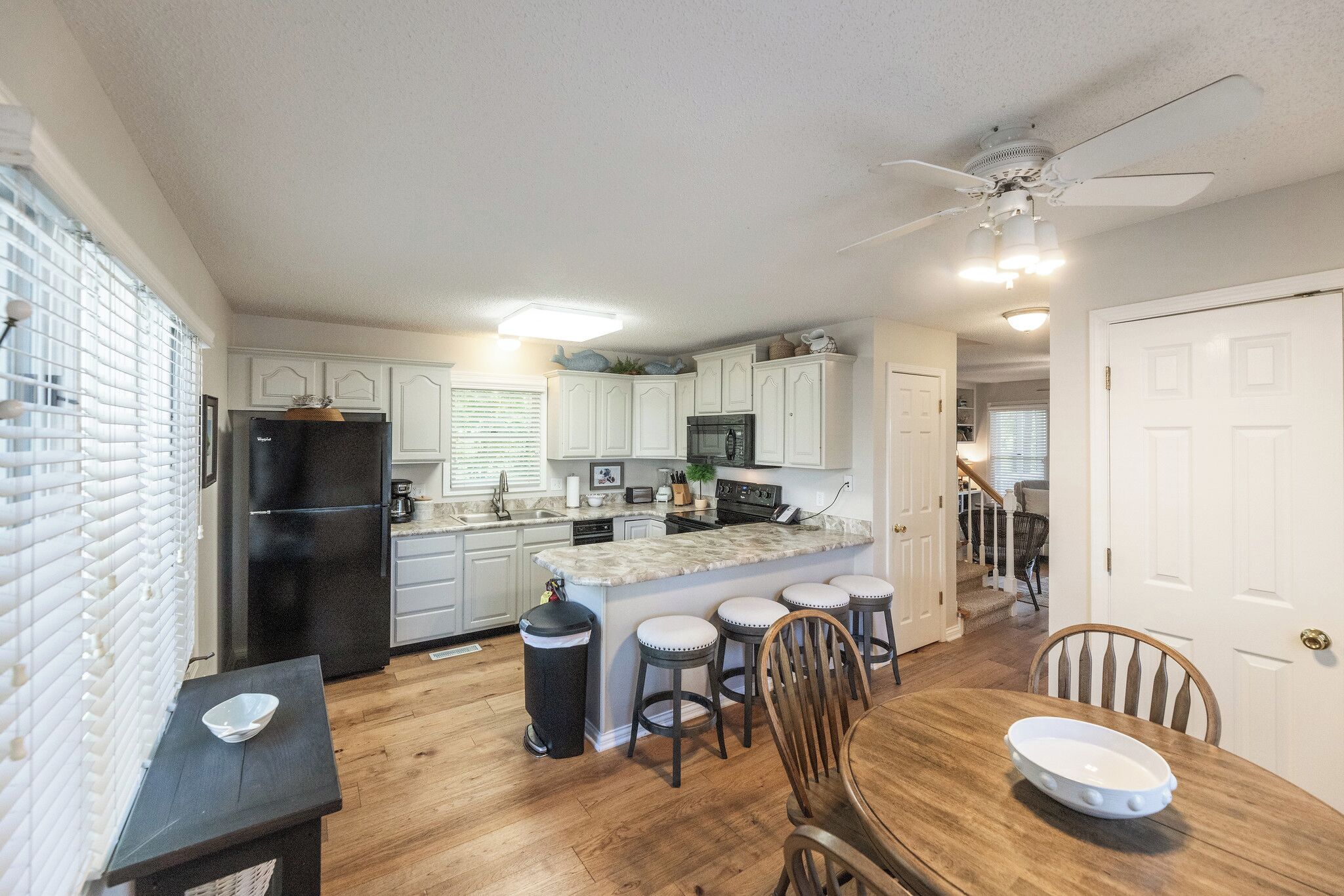 A kitchen with white cabinets, a black refrigerator, a marble island with stools, and a dining table with chairs.