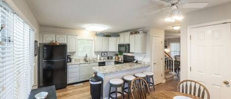 A kitchen with white cabinets, a black refrigerator, a marble island with stools, and a dining table with chairs.