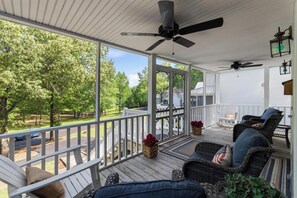 A covered porch with wicker furniture, ceiling fans, and a view of a green landscape.