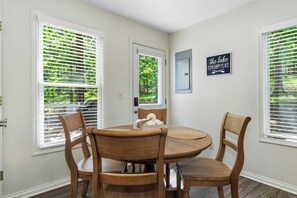 Un coin repas comprenant une table ronde en bois, quatre chaises en bois et une fenĂȘtre avec des stores.