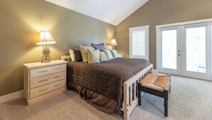 A bedroom with a bed, nightstands, a bench, and a large window with blinds.
