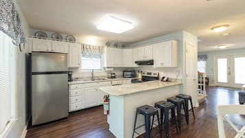 A kitchen with white cabinets, a stainless steel refrigerator, a microwave, a stove, and a sink. There are three stools at the island.