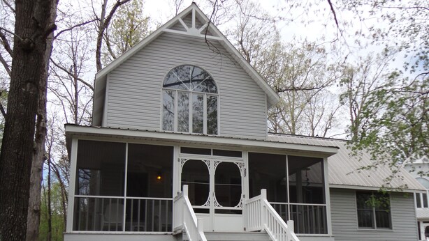 A two-story house with a front porch, a staircase leading to the entrance, and a large arched window above the door.