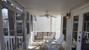 A covered porch with white chairs, a ceiling fan, and a wooden deck.