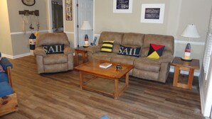 A living room with a brown leather sofa, two armchairs, a coffee table, and a small side table with a lamp.