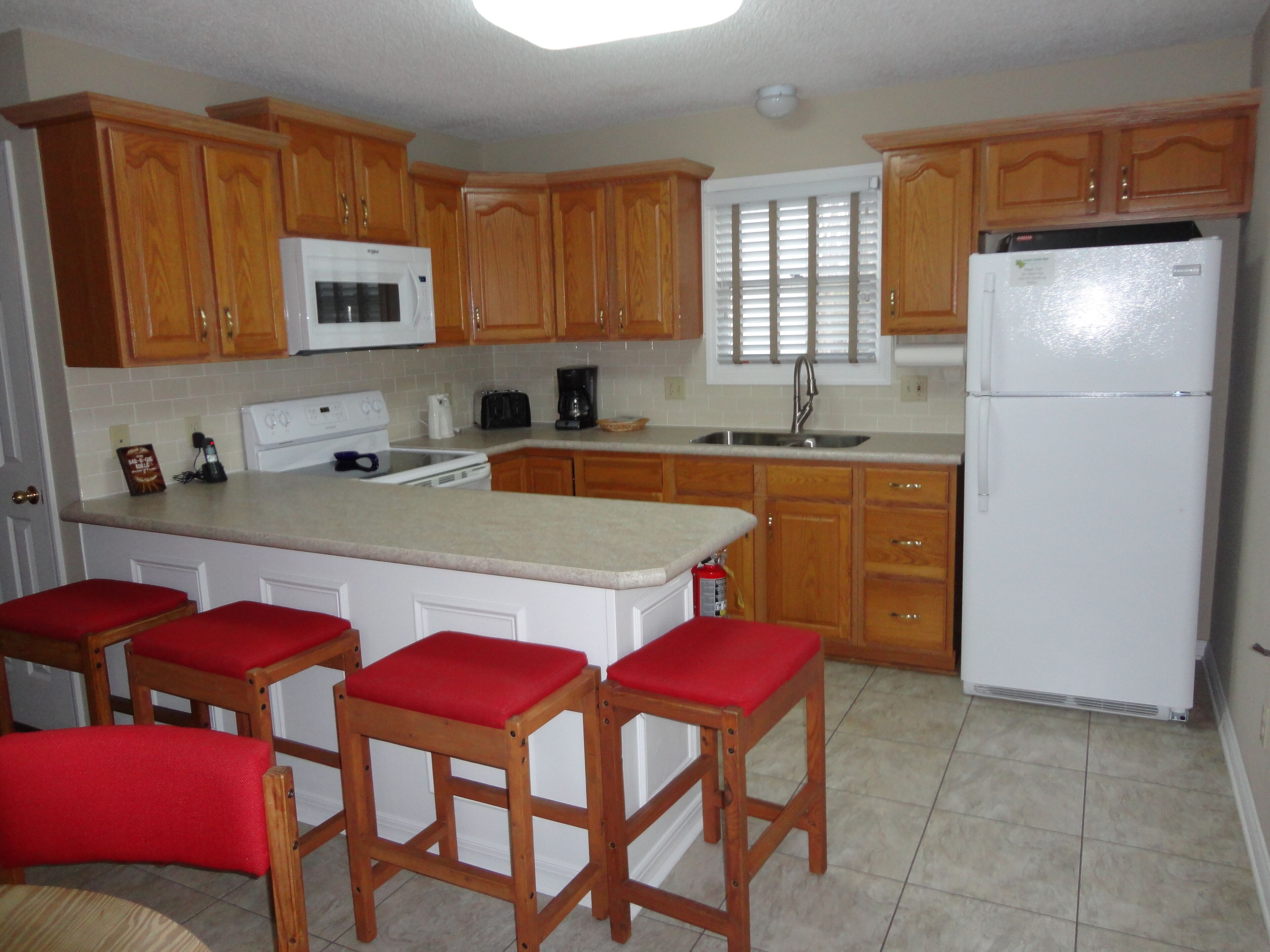 A kitchen with wooden cabinets, a white refrigerator, a microwave, a stove, and red bar stools.