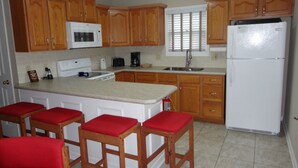 A kitchen with wooden cabinets, a white refrigerator, a microwave, a stove, and red bar stools.