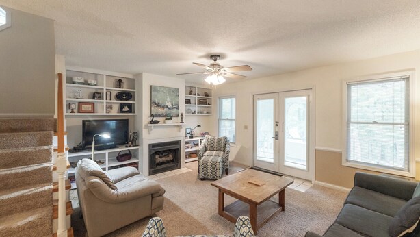A living room with a fireplace, a television, a ceiling fan, and a staircase. - Three Bedroom Hurst Haven Condo (Grand Rivers)