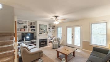 A living room with a fireplace, a television, a ceiling fan, and a staircase.