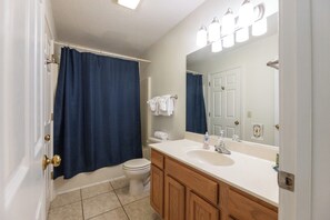 Une salle de bain avec des toilettes blanches, un lavabo avec un miroir et un rideau de douche bleu.