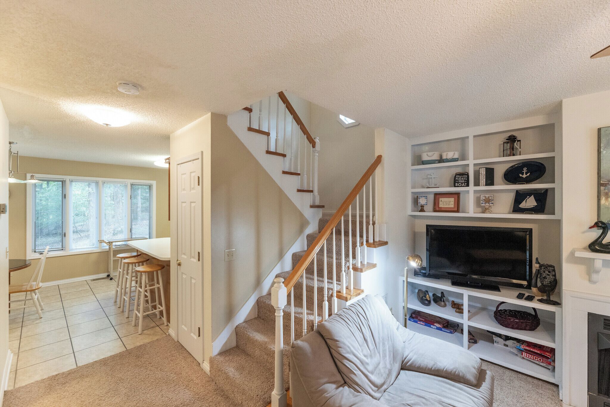 A living room with a beige couch, a TV, and a bookshelf. There is a staircase with wooden railings leading to another room.
