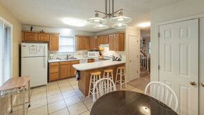 A kitchen with wooden cabinets, a white refrigerator, a microwave, a stove, and a bar stool area. - Three Bedroom Hurst Haven Condo (Grand Rivers)