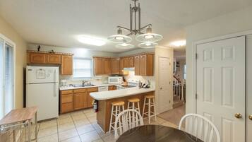 A kitchen with wooden cabinets, a white refrigerator, a microwave, a stove, and a bar stool area.