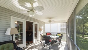 Une véranda couverte avec un ventilateur de plafond, des meubles en osier et une vue sur l’extérieur.