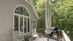 A covered patio with a round table and chairs, a grill, and a large umbrella. - One Bedroom Bayside Condo (Grand Rivers)