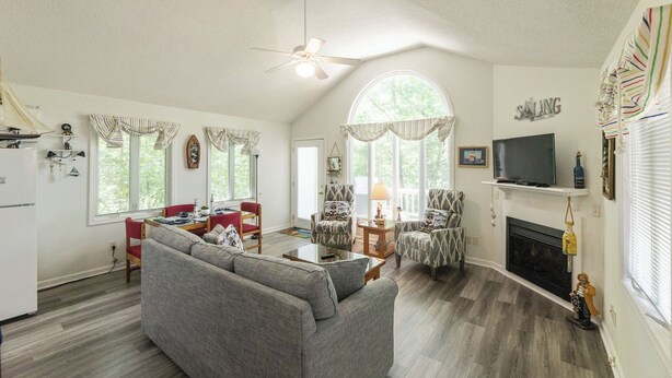 A spacious living room with a gray sofa, a dining area with a red chair, and a fireplace. - One Bedroom Bayside Condo (Grand Rivers)