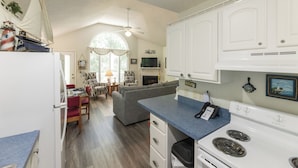 A compact kitchen with white cabinets, a stove, and a dining area with a sofa and chairs. - One Bedroom Bayside Condo (Grand Rivers)
