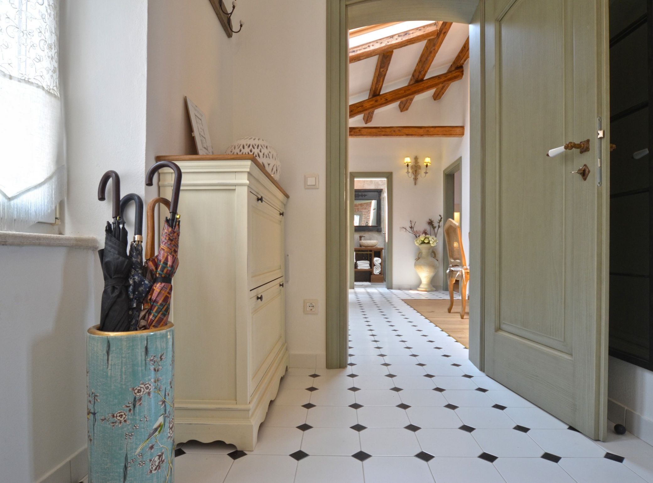 A hallway with a tiled floor, a wooden door, and a cabinet with umbrellas.