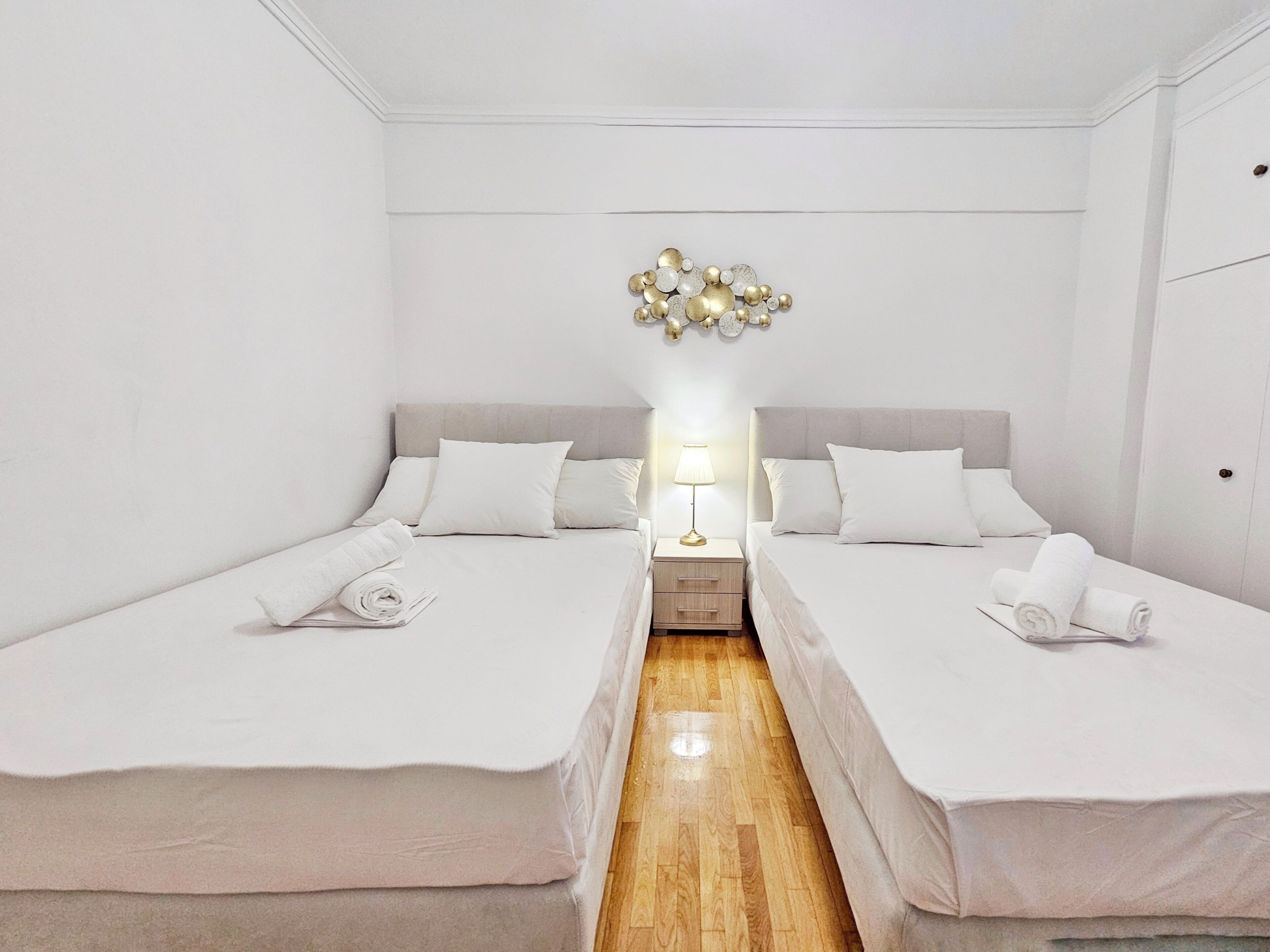 A hotel room with two beds, a wooden floor, and a decorative wall piece above the beds.