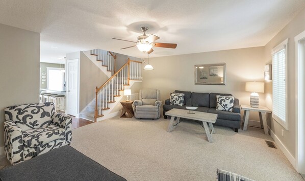 A living room with a staircase, a ceiling fan, a sofa, a chair, and a coffee table. - Executive Two Bedroom Pond View Condo (Grand Rivers)