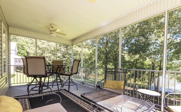 A covered patio with a table and chairs, a bench, and a view of trees and a body of water. - Executive Two Bedroom Pond View Condo (Grand Rivers)