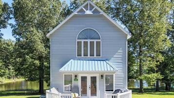 Une maison à deux étages avec un toit bleu, un porche à l’avant et un chemin en briques menant à l’entrée.