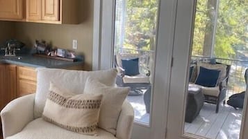 Een gezellige woonkamer met een ronde witte fauteuil, een houten kast en een schuifdeur naar een terras.