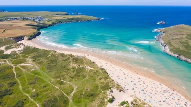 Vue aérienne d’une zone côtière avec une plage, des eaux d’un bleu limpide et des paysages verdoyants.