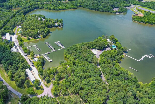 An aerial view of a lakeside property with a marina, parking area, and buildings surrounded by dense greenery.